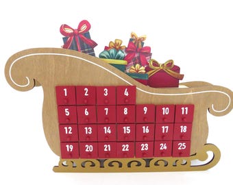 May include: Wooden Christmas advent calendar in the shape of a sleigh. The sleigh is filled with colorful gift boxes and has 25 small red drawers numbered 1-25. A festive holiday decoration.