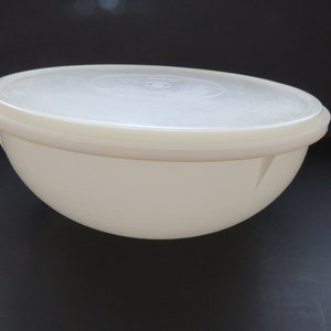 May include: A large, off-white plastic mixing bowl with a matching lid. The bowl has a rounded shape and a smooth surface. The lid is translucent and fits snugly on top. Ideal for food preparation and storage.