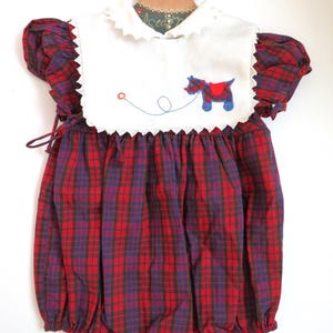 May include: Vintage red, blue, and green plaid baby romper with a white bib collar. The collar features a horse applique with a red saddle and blue legs. The romper has short sleeves and a gathered bottom.