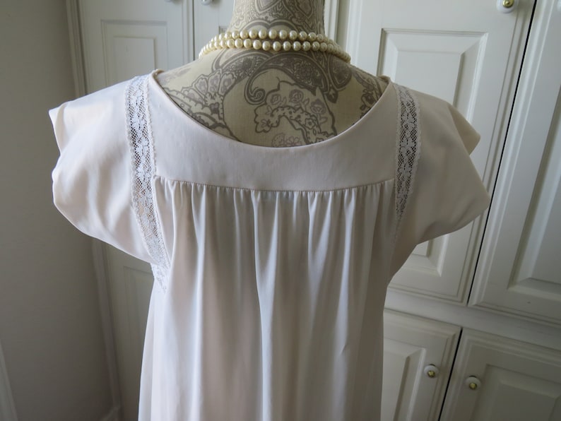 May include: A white nightgown with lace trim on the sleeves. The nightgown has a scoop neck and a gathered bodice.