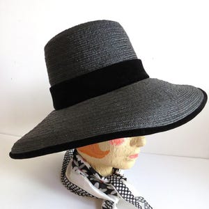 May include: A wide-brimmed black straw hat with a black velvet band. The hat is sitting on a mannequin head.