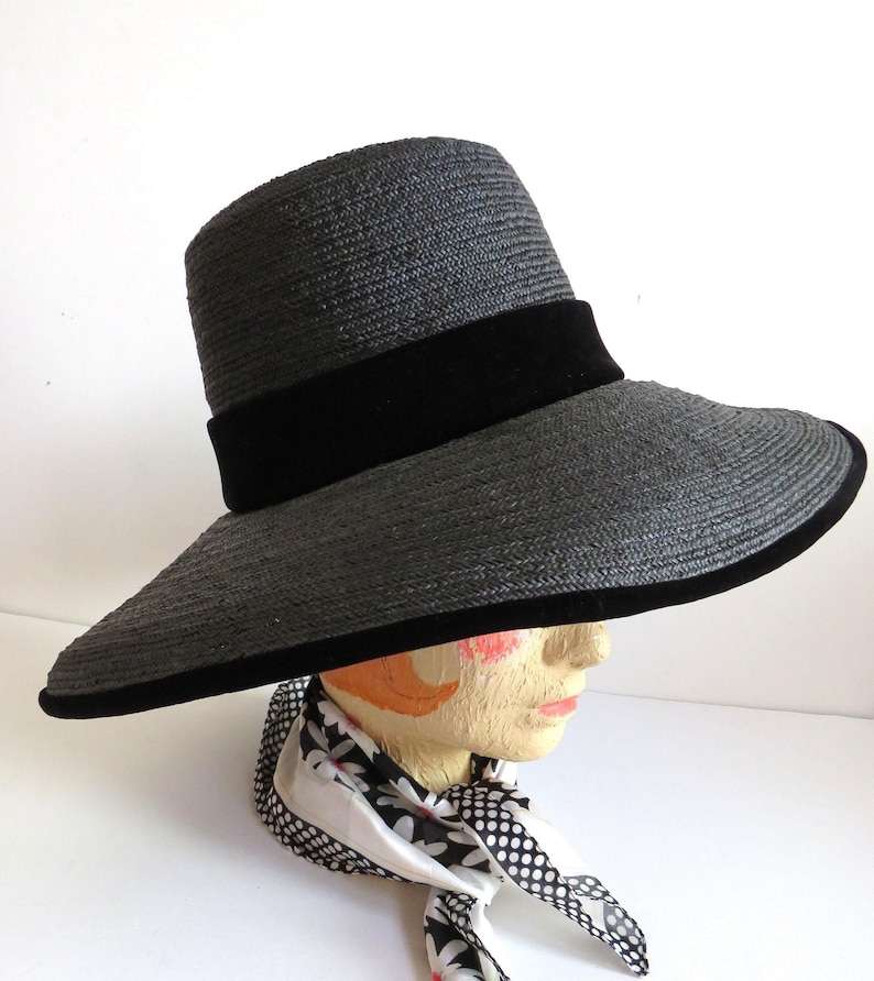 May include: A wide-brimmed black straw hat with a black velvet band. The hat is sitting on a mannequin head.
