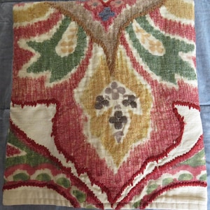 May include: A decorative pillow with a colorful floral pattern in shades of red, green, yellow, and brown. The pillow has a white background and a textured fabric.