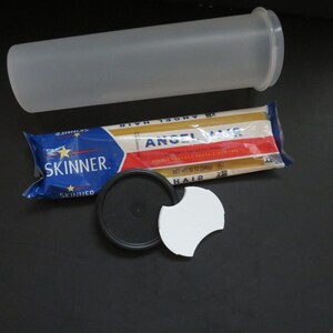 Könnte beinhalten: Ein durchsichtiges Plastikrohr mit einem weißen Deckel, eine Packung Angel Hair Pasta von Skinner, ein schwarzer Deckel und ein weißes Plastikteil.