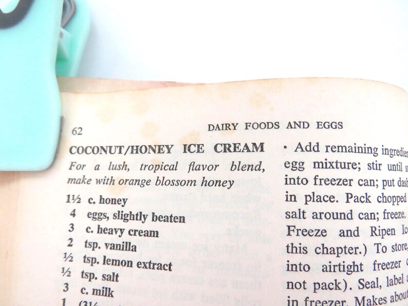 May include: A page from a cookbook titled Dairy Foods and Eggs, featuring a recipe for Coconut/Honey Ice Cream. The page is held by a light mint green plastic clip. The text lists ingredients including honey, eggs, heavy cream, vanilla, and milk.