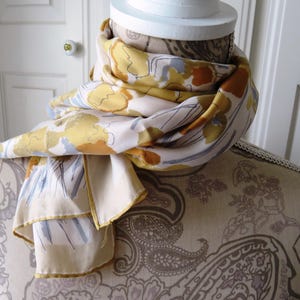 Peut inclure: Un mannequin blanc portant une &eacute;charpe &agrave; motifs floraux jaunes, bruns et bleus. L'&eacute;charpe est drap&eacute; autour du cou et des &eacute;paules du mannequin.