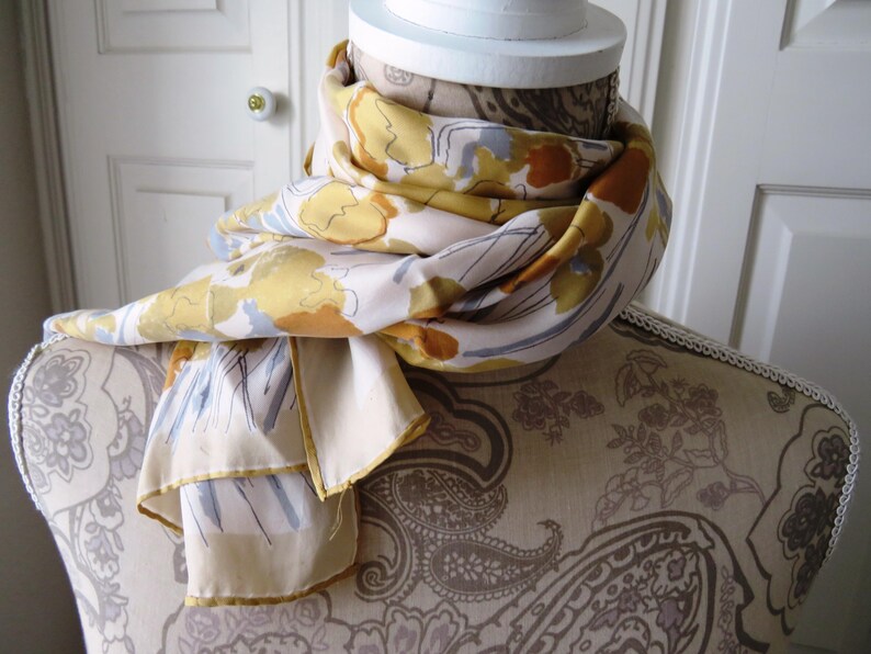 Peut inclure: Un mannequin blanc portant une &eacute;charpe &agrave; motifs floraux jaunes, bruns et bleus. L'&eacute;charpe est drap&eacute; autour du cou et des &eacute;paules du mannequin.