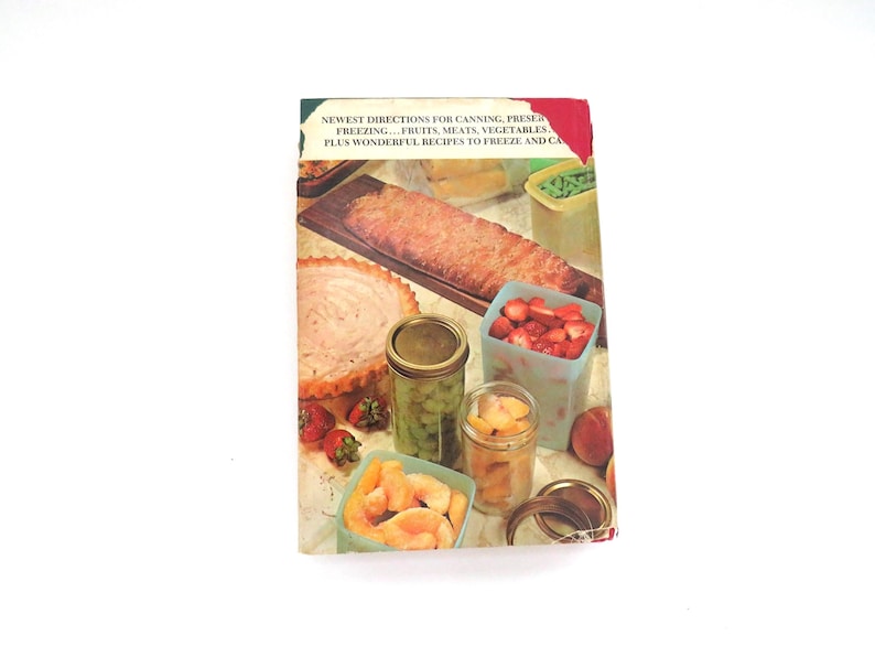 May include: A vintage cookbook with a rectangular cover featuring a color photograph of various preserved foods, including a loaf, a pie, and glass jars filled with fruits and vegetables. The text reads: NEWEST DIRECTIONS FOR CANNING, PRESERVING, FREEZING... FRUITS, MEATS, VEGETABLES, PLUS WONDERFUL RECIPES TO FREEZE AND CAN.