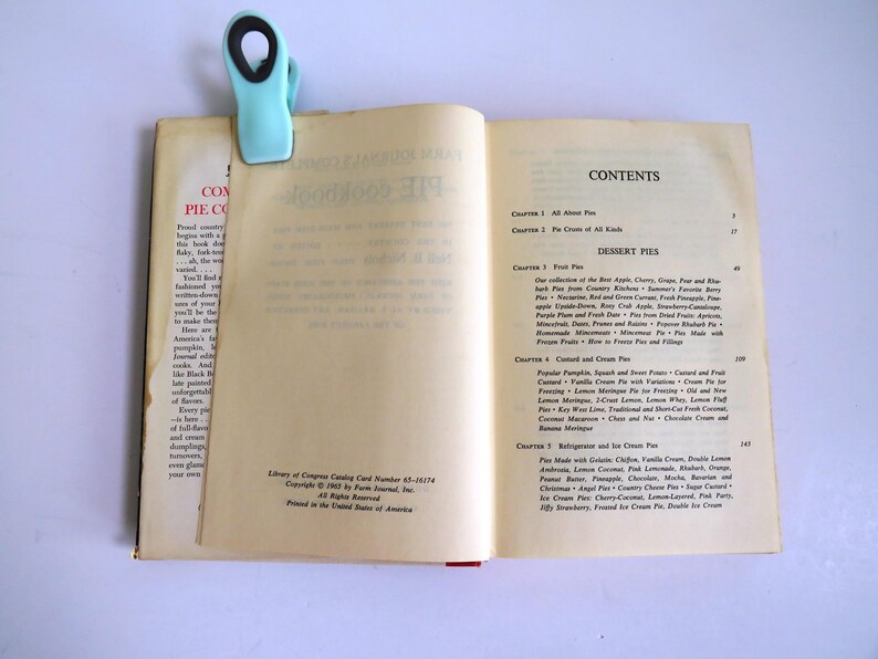 Puede incluir: Un libro abierto con un clip de carpeta azul en la p&aacute;gina superior. El libro se titula "Complete Pie Cookbook" y la p&aacute;gina de contenido enumera diferentes tipos de tartas, incluidas tartas de frutas, tartas de crema y tartas de refrigerador.