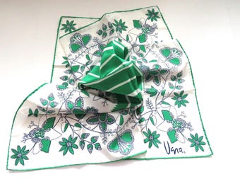 Op de afbeelding: Een witte zijden sjaal met een groen bloemenpatroon en een groen-wit gestreept ontwerp. De sjaal is gevouwen en heeft het woord "Una" gedrukt in de rechterbenedenhoek.
