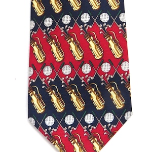 May include: A necktie featuring a repeating pattern of yellow golf bags, white golf balls, and crossed golf clubs arranged in diagonal rows against alternating dark navy blue and bright red diamond-shaped background sections.