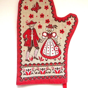 Puede incluir: Manopla de horno roja y beige con un diseño de arte popular. La manopla presenta un borde rojo festoneado y un diseño de una pareja con ropa tradicional, flores rojas y una mariposa. Se adjunta un lazo rojo.