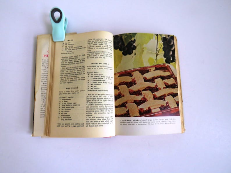 Puede incluir: Un libro de cocina vintage abierto en una receta para "Pressed No-Apple Pie". La receta incluye ingredientes como yemas de huevo, mantequilla, az&uacute;car y canela. La p&aacute;gina tambi&eacute;n presenta una foto de un pastel con una corteza de celos&iacute;a, una corteza marr&oacute;n y un relleno rojo oscuro.