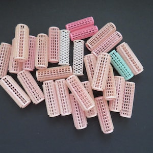 May include: A collection of cylindrical hair rollers in various shades of light pink, with one white roller and one light blue roller. Each roller features a grid-like plastic mesh design with a textured surface for gripping hair strands.