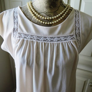 May include: A white, sleeveless nightgown with a lace trim around the neckline and shoulders. The nightgown is gathered at the bust and has a simple, classic design.