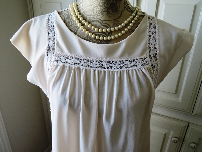 May include: A white, sleeveless nightgown with a lace trim around the neckline and shoulders. The nightgown is gathered at the bust and has a simple, classic design.