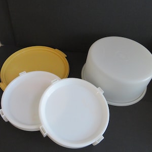 May include: A selection of white and yellow plastic food storage containers. The set includes a large white container with a lid, two white lids, and a yellow lid. The containers are on a dark surface.
