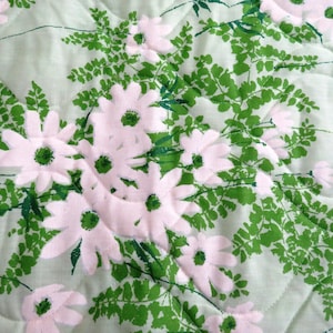 May include: A quilted fabric featuring a repeating pattern of large white daisy-like flowers with green centers and green fern-like leaves on a light green background. The fabric has a soft, textured appearance.