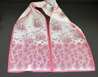 May include: A white silk scarf with a pink floral print. The scarf has a pink border and features a design of pink and white flowers.
