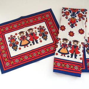 Può includere: Due pezzi tessili vintage con un design di arte popolare. Uno è rettangolare, l'altro piegato. Entrambi presentano uno sfondo bianco con un bordo rosso e blu. Il design include figure stilizzate in abiti tradizionali, fiori e cuori.