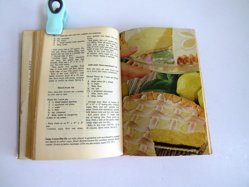 Puede incluir: Libro de cocina abierto con una receta de pastel de melocot&oacute;n y ciruela y una foto de un pastel de merengue de lim&oacute;n con una corteza de celos&iacute;a. La receta incluye ingredientes como melocotones en rodajas, ciruelas rojas, az&uacute;car, harina y mantequilla. El pastel es de un hermoso color amarillo dorado con una cobertura de merengue blanco.