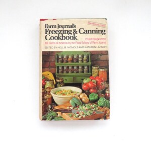 May include: A hardcover cookbook titled Farm Journal's Freezing & Canning Cookbook, edited by Nell B. Nichols and Kathryn Larson. The cover features a green spice rack, jars of preserved food, a bowl of vegetables, and chopped produce on a board.