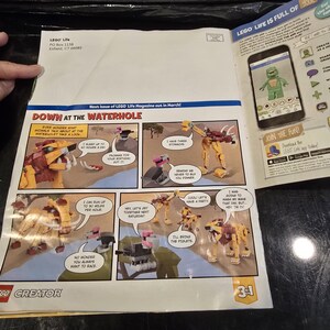 May include: A LEGO Creator 3-in-1 magazine page featuring a comic strip titled Down at the Waterhole with various animal figures. The page includes text, a smartphone graphic showing a green character, and the LEGO Life logo in the top corner.