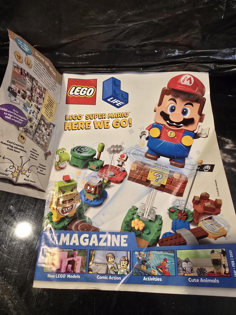 May include: A LEGO Life magazine featuring Super Mario on the cover. The cover displays a LEGO Mario figure, various Super Mario characters, and building sets. Text includes LEGO Life, LEGO Super Mario Here We Go!, and The Magazine. The bottom shows small panels labeled New LEGO Models, Comic Action, Activities, and Cute Animals.