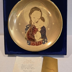 Op de afbeelding: Een goudkleurige decoratieve plaat met een illustratie van moeder en kind. De plaat heeft een gouden rand en een centraal beeld van een moeder en kind in een liefdevolle omhelzing. De plaat is met de hand beschilderd op fijn Beiers porselein en wordt geleverd met een certificaat.
