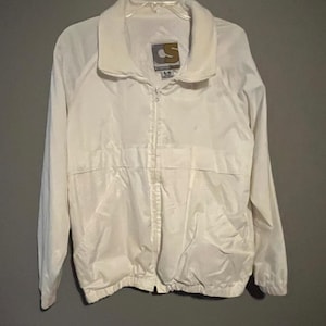 May include: A white, lightweight jacket with a full zipper closure and a collared neckline. The jacket features a small logo on the upper left chest area. The jacket has long sleeves and a drawstring hem. The jacket is made of a shiny material.