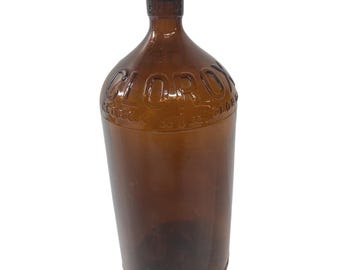 May include: A vintage brown glass bottle with the embossed word "CLOROX" on the front. The bottle has a cork stopper and a rounded shoulder. The bottle is approximately 12 inches tall.