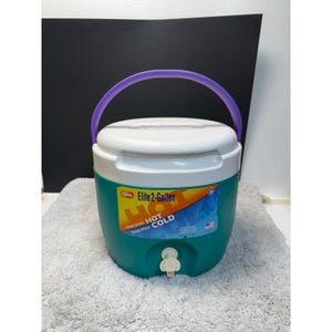 Puede incluir: Una nevera portátil Igloo Elite de 7,5 litros, verde azulado y blanca, con un asa morada. La nevera tiene una tapa blanca y un grifo para dispensar bebidas. La etiqueta dice "Hot Cold" y "Keeps drinks Keeps drinks".