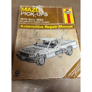 Könnte beinhalten: Ein braunes Haynes Automotive Repair Manual für Mazda Pick-Ups von 1972 bis 1993. Das Cover zeigt eine detaillierte Illustration eines weißen Pick-up-Trucks mit Schnittansichten von Motor und Fahrgestell. Das Handbuch ist auf Recyclingpapier gedruckt.