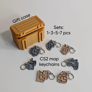 Könnte beinhalten: Ein beigefarbener rechteckiger Geschenkkoffer mit Deckel und sechs Schlüsselanhängern in Form von Spielkarten in Grau- und Beigetönen. Der Text auf dem Bild lautet Gift case, Sets: 1-3-5-7 pcs und CS2 map keychains. Jeder Anhänger hat einen Metallring.