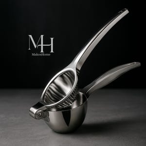 Op de afbeelding: Een roestvrijstalen citruspers met een hendel. De pers heeft een komvormige basis en een geperforeerde bovenkant voor het persen van citrusvruchten. Het logo "MH MakosHome" is zichtbaar.