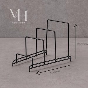 Pode incluir: Organizador de cozinha em metal preto, com 17,5 cm de largura e 13,5 cm de altura, com três divisórias verticais. O organizador tem uma base retangular e foi projetado para guardar tábuas de corte ou outros itens de cozinha. A marca "MakosHome" é visível.