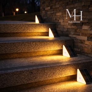 Peut inclure: Des lampes d'escalier solaires éclairent un escalier en pierre au crépuscule. Les lumières triangulaires ont un panneau solaire noir et une lumière blanche vive. Les lumières sont placées sur chaque marche, créant une lueur chaleureuse. La marque "MakosHome" est visible.