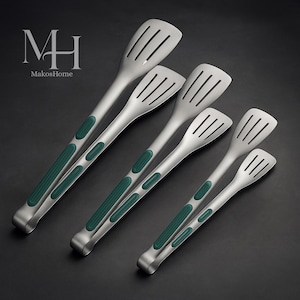 Puede incluir: Juego de pinzas de cocina de acero inoxidable con mangos de silicona verde. Las pinzas tienen cabezas ranuradas y están dispuestas en diagonal sobre un fondo oscuro. El logotipo "MH MakosHome" está en la esquina superior izquierda.