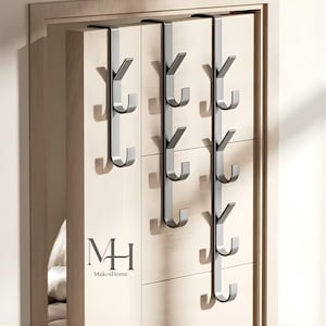 May include: Silver metal over-the-door hooks with a modern design. The hooks are attached to a light-colored wooden door. The hooks are designed to hang items and are a space-saving storage solution. The logo "MH MakosHome" is visible.
