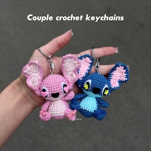 May include: Two crochet keychains, one pink and one blue, each featuring a cartoon character design. The pink keychain has heart-shaped eyes, while the blue one has star-shaped eyes. The text "Couple crochet keychains" is at the top.
