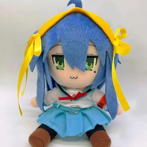 以下が含まれることがあります： 青い髪と緑の目をしたぬいぐるみ。白いシャツ、水色のスカート、茶色の靴を履いています。黄色いリボン付きのヘアバンドをしており、座っています。