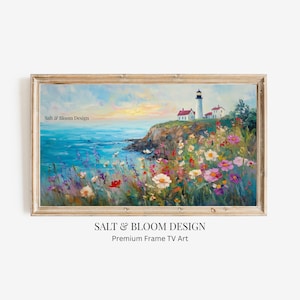 Puede incluir: Una pintura de paisaje enmarcada representa una escena costera con un faro, flores silvestres y el océano. La obra de arte presenta un faro blanco con una parte superior negra, situado en un acantilado con vistas al océano azul. El primer plano está lleno de coloridas flores silvestres. El texto "Salt & Bloom Design" es visible.
