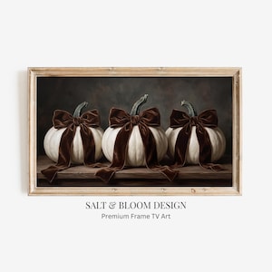 May include: A rectangular framed wall art piece featuring three white pumpkins sitting on a wooden surface. Each pumpkin is adorned with a large, dark brown velvet bow tied around its stem. The text SALT & BLOOM DESIGN Premium Frame TV Art appears below.