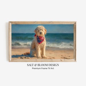 May include: A framed print of a golden doodle dog sitting on a sandy beach, wearing a red, white, and blue bandana. The background features ocean waves and a blue sky. The frame is made of light-colored wood. The text "SALT & BLOOM DESIGN" is at the bottom.