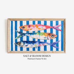 Puede incluir: Obra de arte enmarcada con tres peces coloridos pintados en estilo impresionista. Los peces están dispuestos horizontalmente sobre un fondo de rayas verticales azules y blancas. El marco es de color madera clara. El texto "SALT & BLOOM DESIGN" está en la parte inferior.