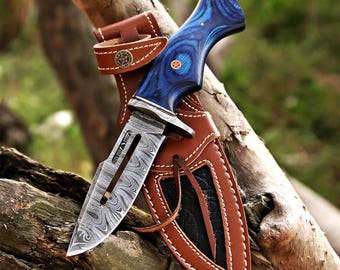 May include: A Damascus steel hunting knife with a blue wood handle and a brown leather sheath. The knife blade has a unique pattern, and the sheath features decorative stitching and a belt loop.