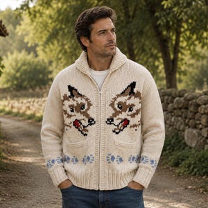 May include: A cream-colored knit zip-up cardigan featuring a shawl collar and two front pockets. The garment displays two symmetrical wolf head designs in brown, black, and red, with a row of light blue paw prints along the bottom hem.