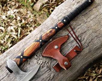 May include: A hand axe with a polished steel blade and a wooden handle wrapped in black leather strips secured with brass rivets. The axe includes a brown leather sheath with a snap button closure and a leather cord for attachment or hanging.