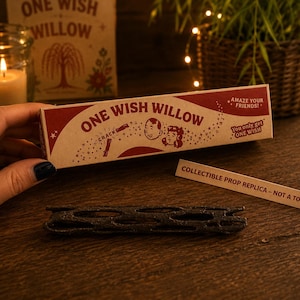 May include: A rectangular cardboard box labeled One Wish Willow with red and tan graphics, featuring illustrations of two faces and the text Amaze your friends and You only get one wish. A dark brown, porous, cylindrical stick lies below.