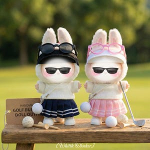 May include: Two plush rabbit dolls dressed in golf attire. The left doll wears a black visor, black sunglasses, a white sweater, and a navy pleated skirt. The right doll wears a pink visor, pink glasses, a white sweater, and a pink pleated skirt.